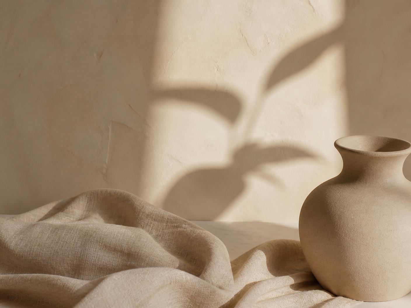 Soft neutral linen and a ceramic vessel in warm daylight